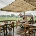 Terrasse de guinguette à la ferme sous la pluie avec des clients attablés sous une bâche en toile