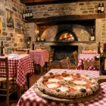 Salle d'une pizzeria italienne en Bourgogne avec four à bois en pierre, tables à nappes à carreaux rouges et blancs, et pizza napolitaine posée sur une pelle en bois au premier plan